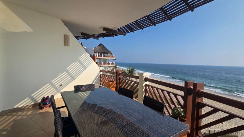 Balcony overlooking ocean, table with chairs, wood railing, blue sky.
