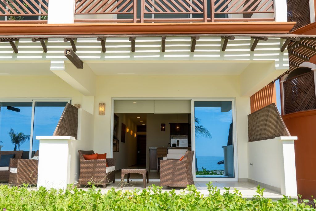 Exterior of a resort suite with patio, wicker furniture, and ocean view through sliding glass doors.