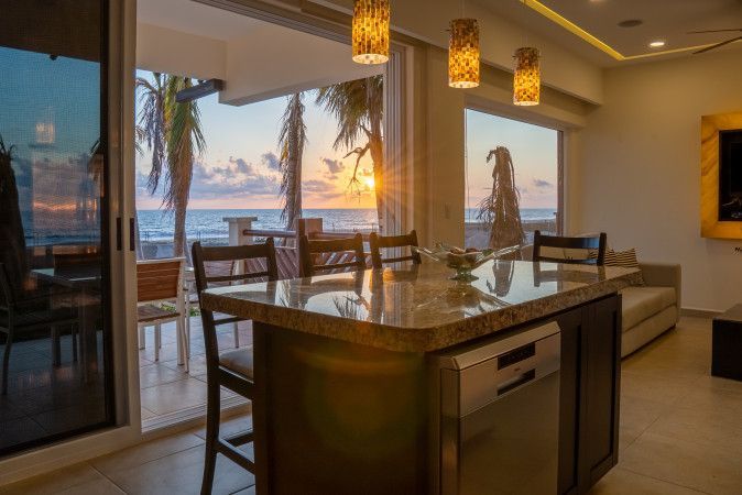Kitchen with island, open to a balcony with ocean view at sunset.
