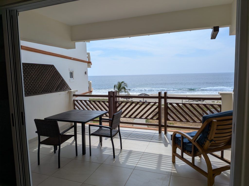 Balcony overlooking ocean; table and chairs, wooden railing.