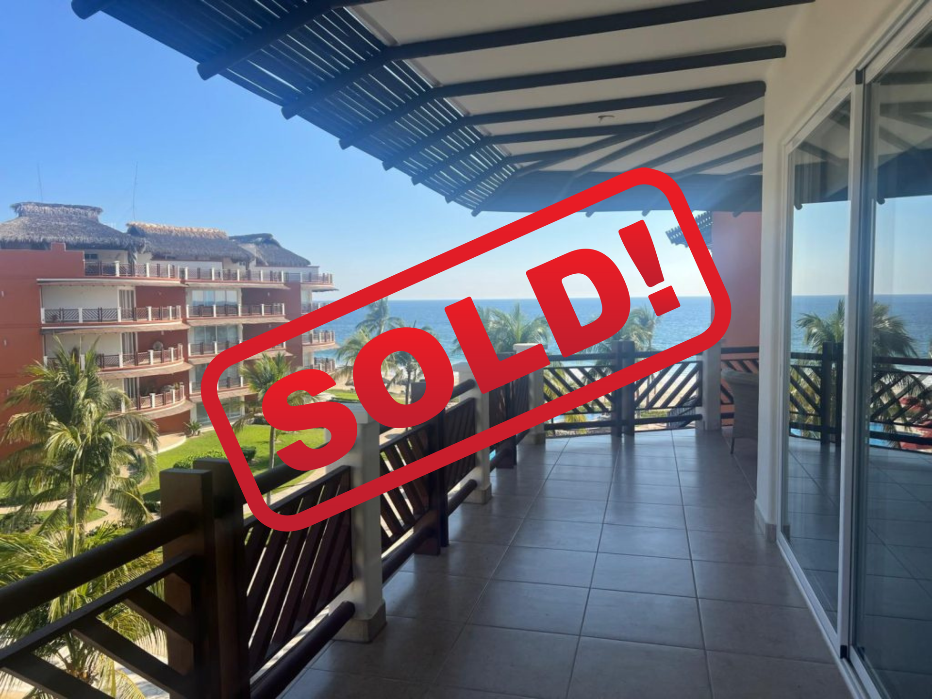 Balcony view of ocean, "SOLD" stamp, condos in background, blue sky.