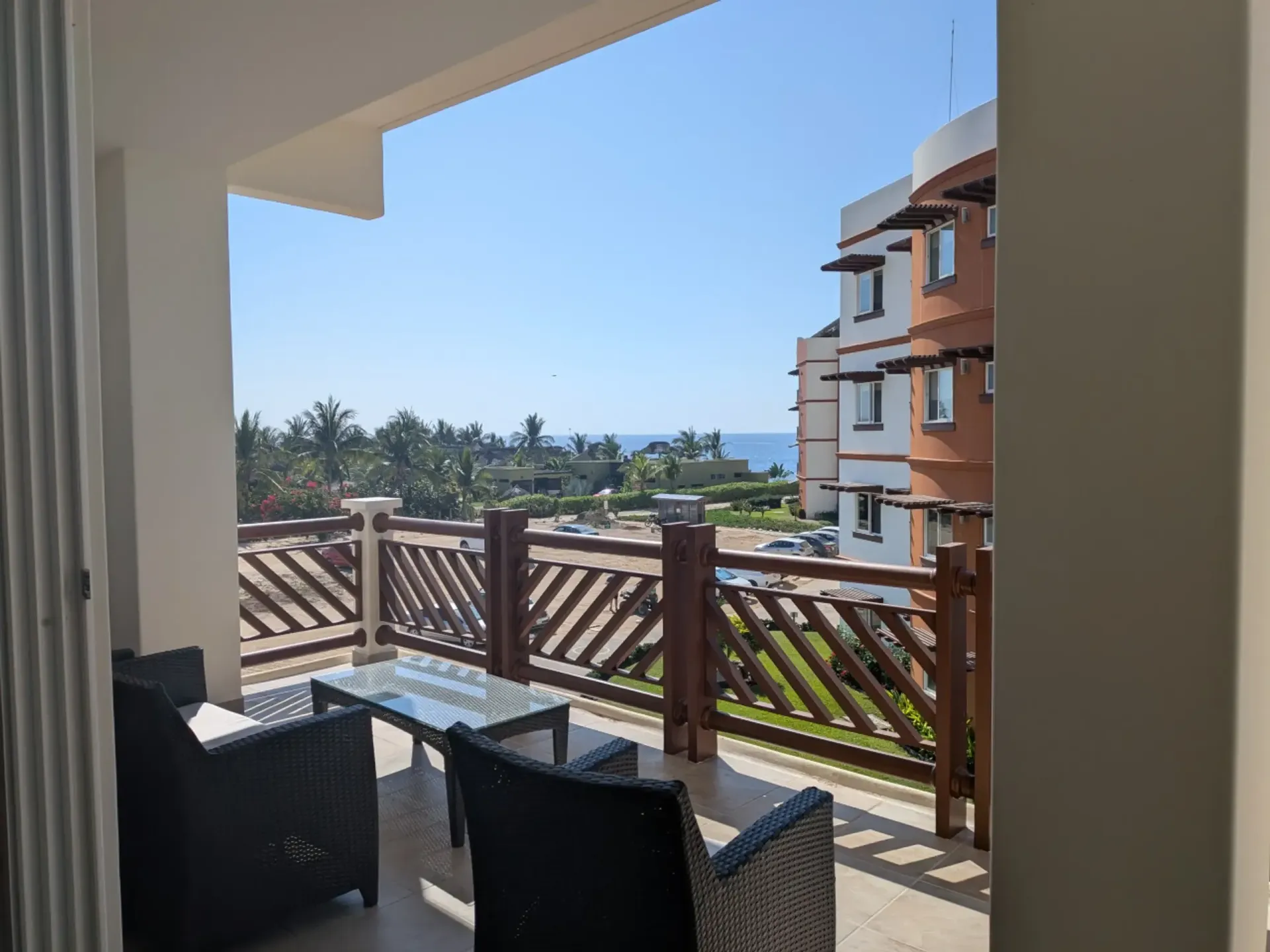 Balcony with wicker chairs overlooking a palm-lined seaside view and blue sky