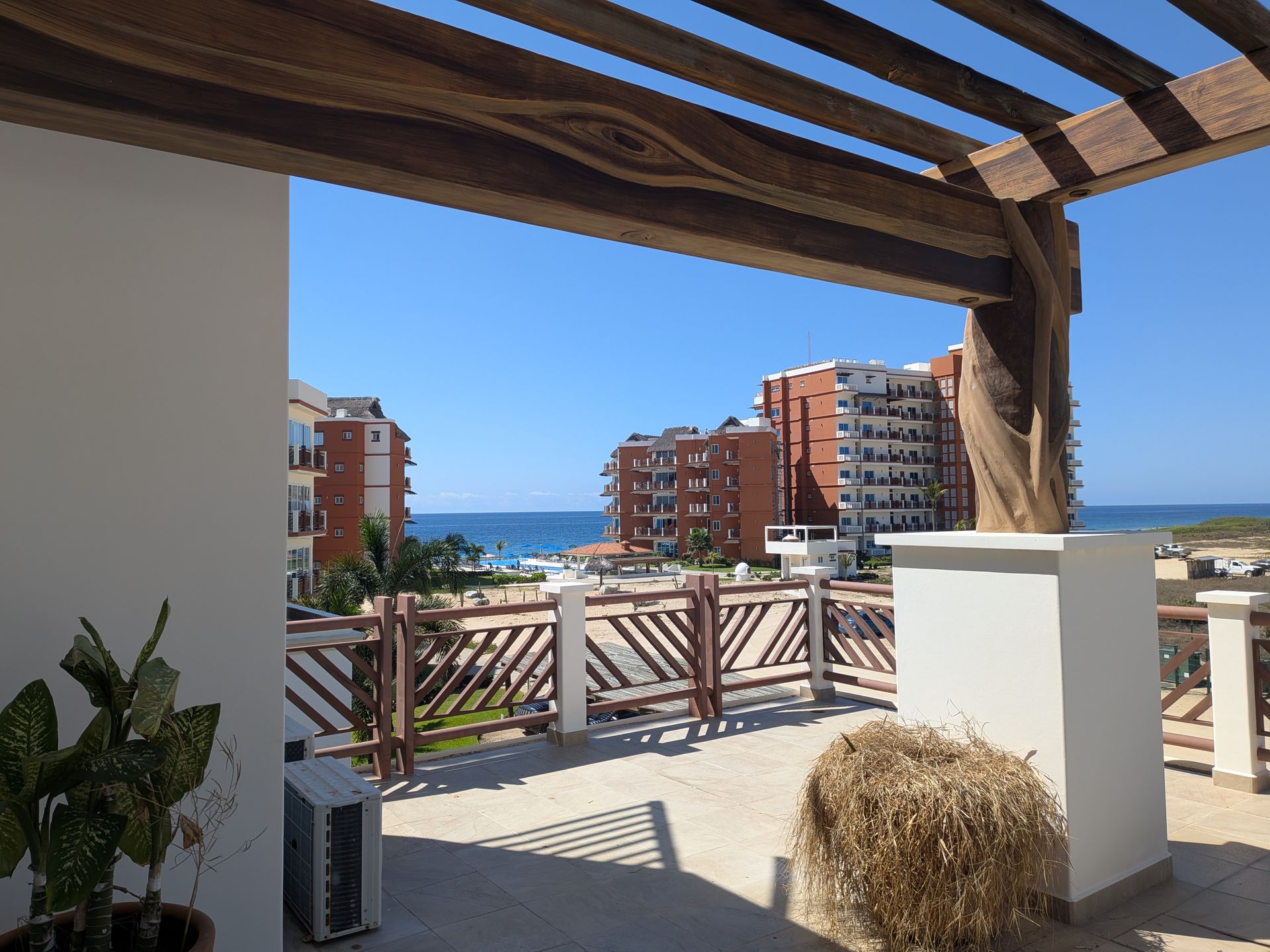 Balcony overlooking the sea with wooden pergola, potted plants, and apartment buildings in the background