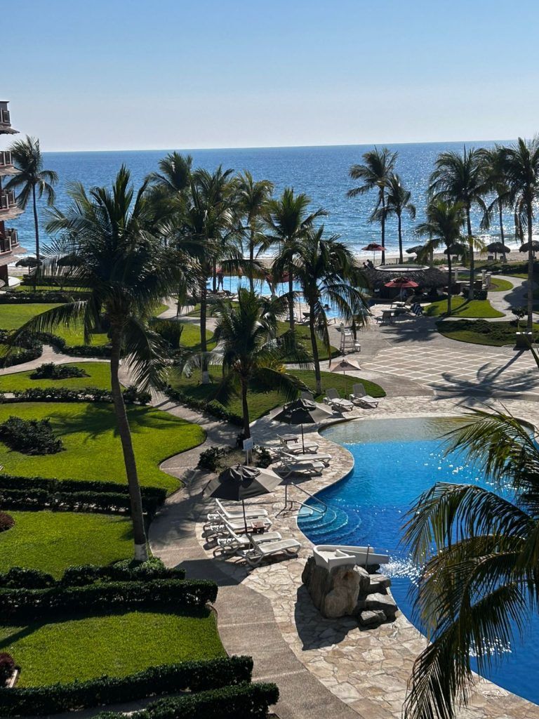 Tropical resort pool with palm trees, white lounge chairs, and ocean view under a clear sky