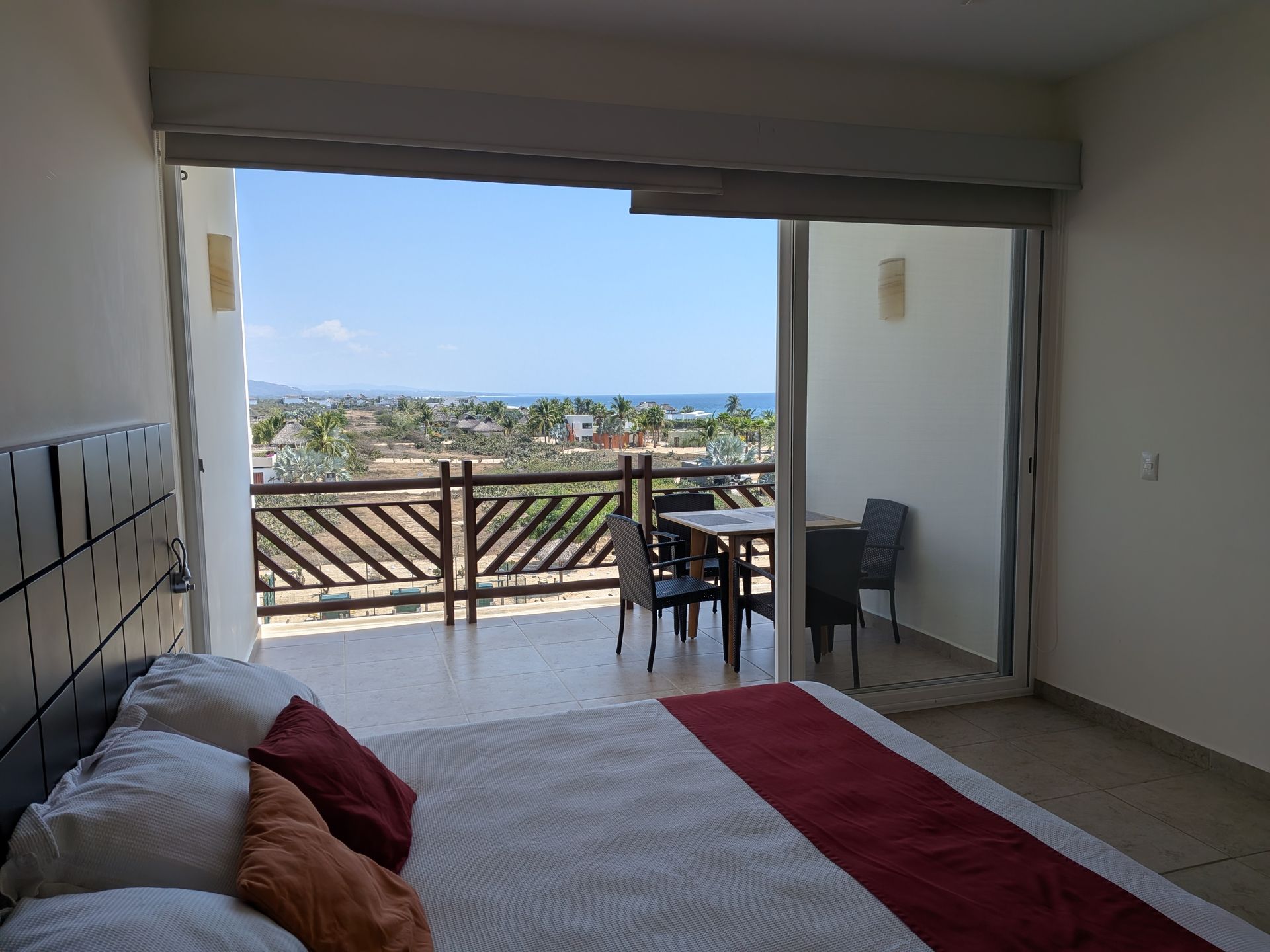 Bedroom opening to a balcony with a sea view, table and chairs, and a bed with a red runner.
