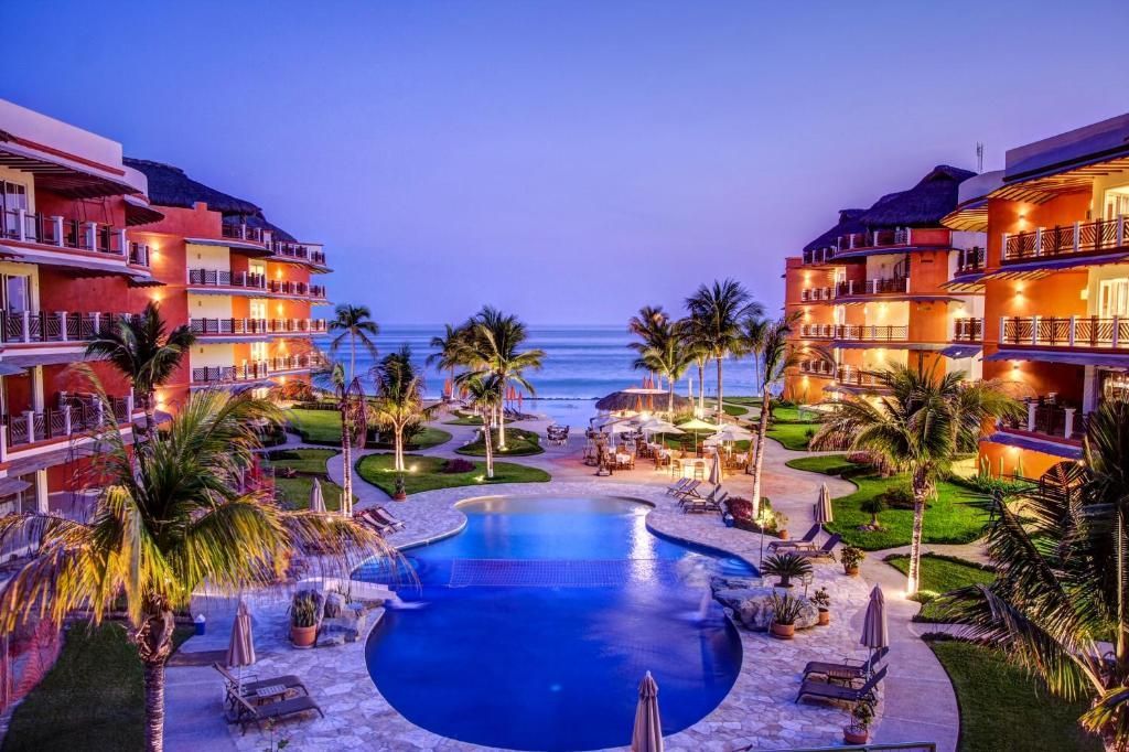 Resort with pool, palm trees, buildings, and beach at dusk.