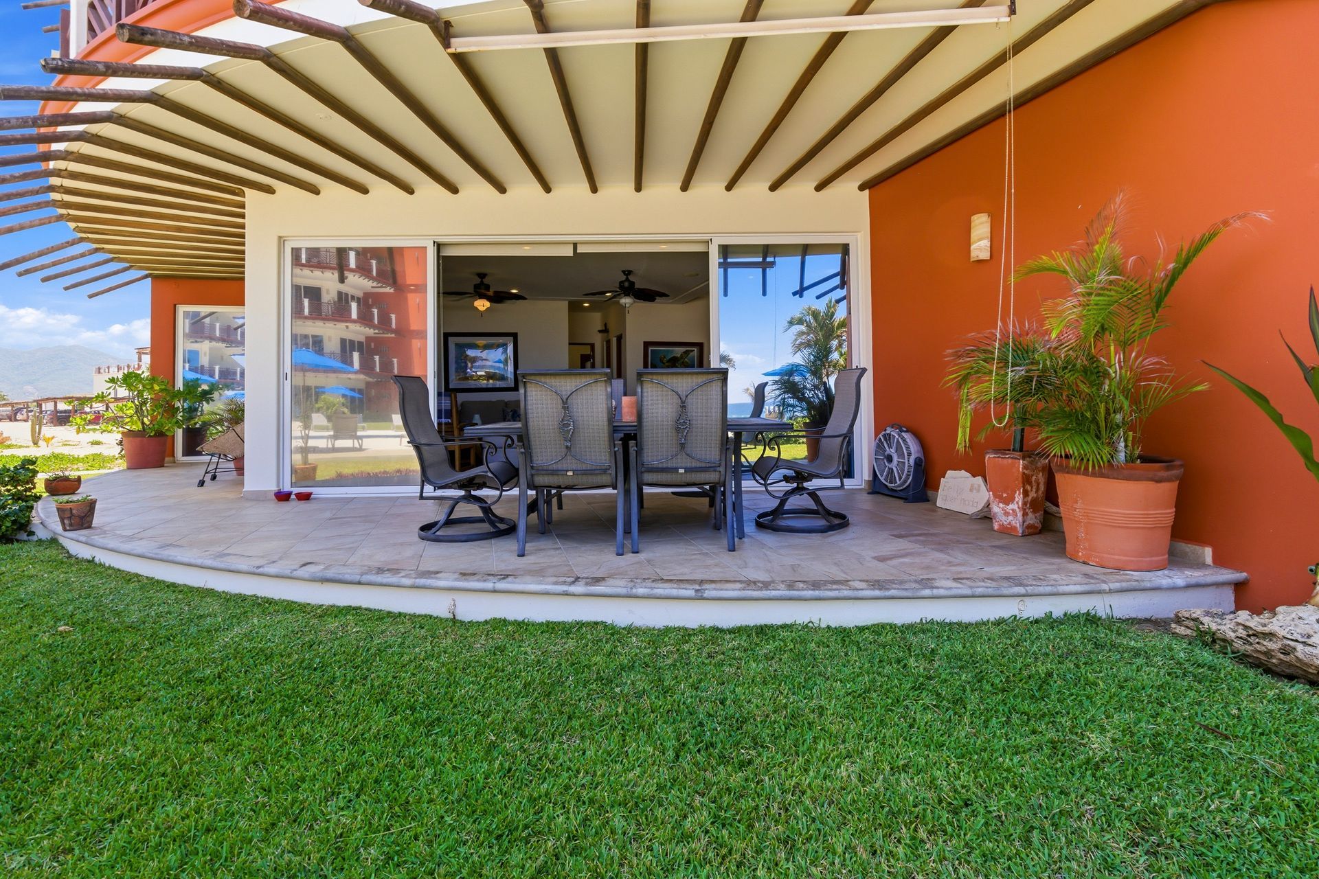 Covered patio with dining table, chairs, and potted plants beside a green lawn