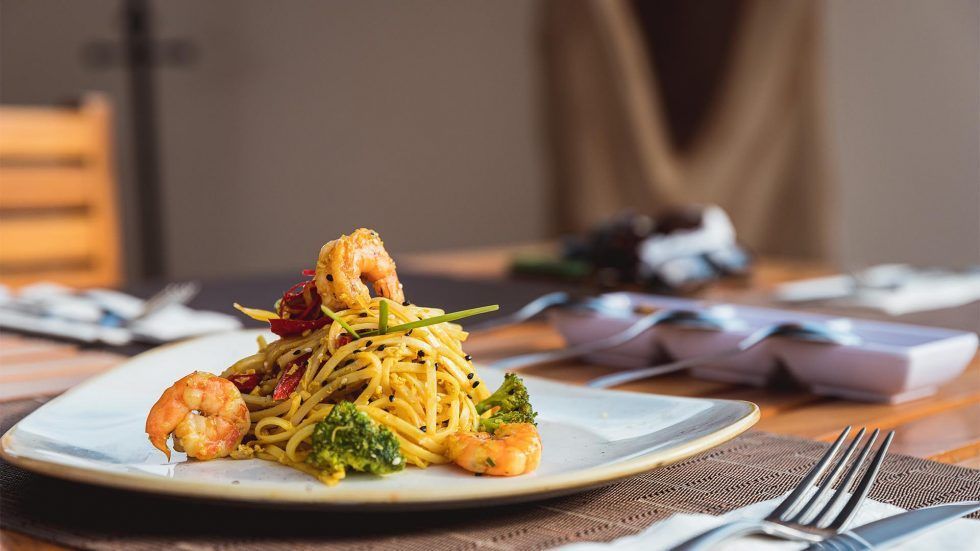 Plate of pasta with shrimp and herbs on a restaurant table, with utensils and napkins nearby