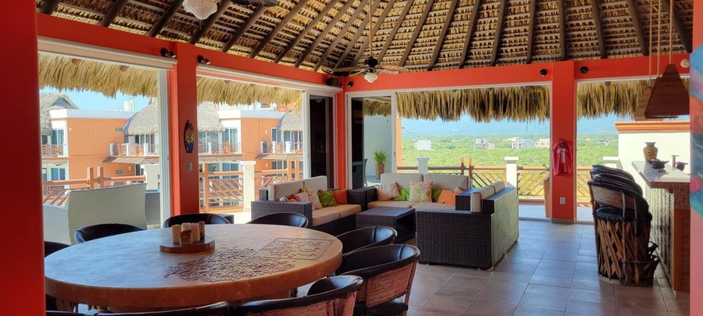 Open-air dining area with a thatched roof, orange walls, and ocean view.