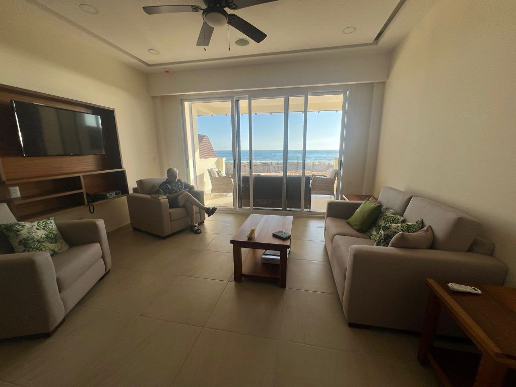 Living room with ocean view, beige sofas, coffee table, person seated.