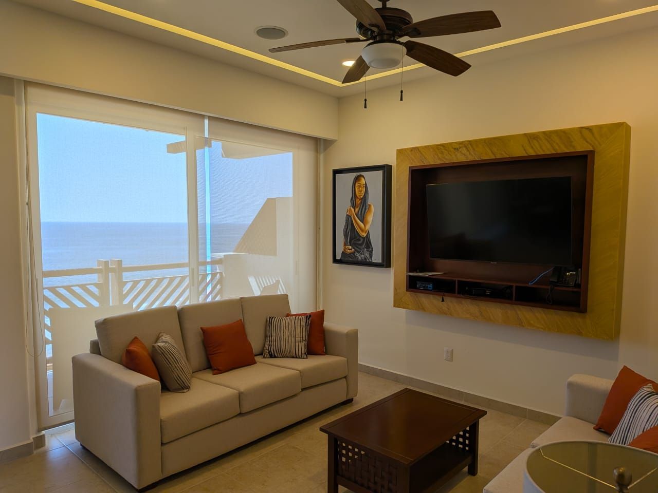 Living room with sofa, wall-mounted TV, coffee table, and ocean view through sliding glass doors
