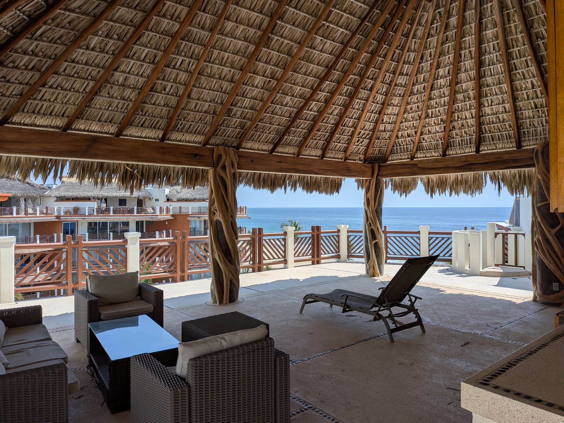 Thatched beachfront lounge with wicker chairs, shaded seating, and ocean view