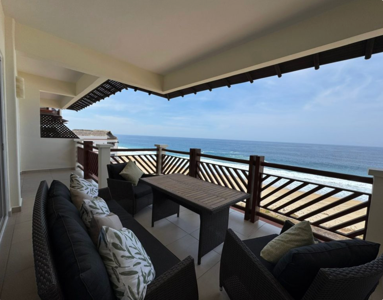 Balcony with wicker furniture overlooking the ocean. Blue sky, water, and brown wooden accents.