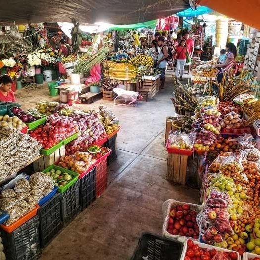 Open-air market stall with colorful fruits and vegetables arranged on tables under a canopy