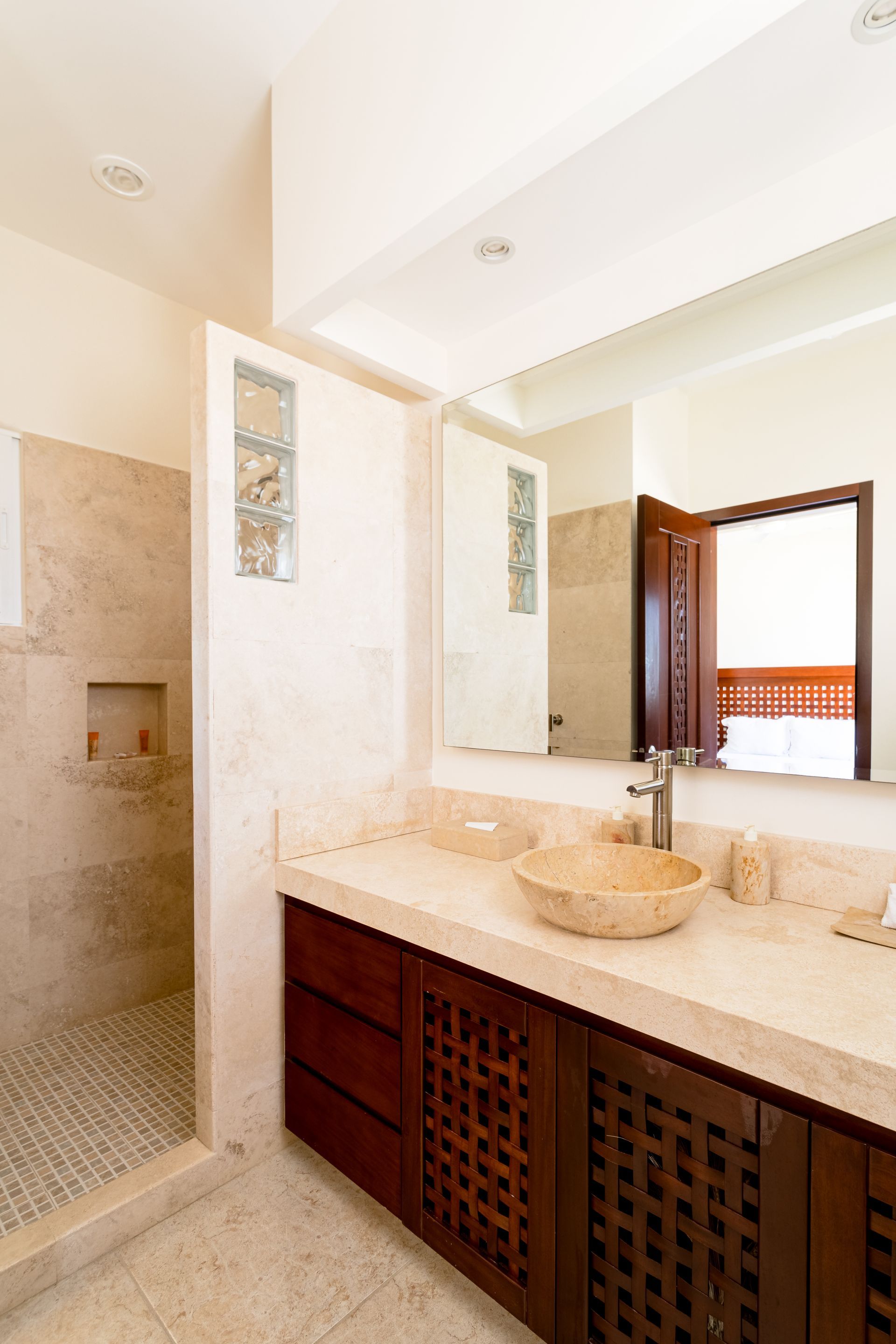 Bright bathroom vanity with cream countertop, round sink, wood cabinets, and mirror beside a shower stall.