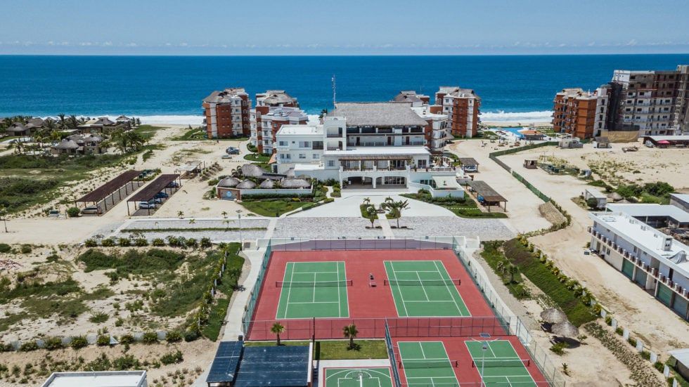 Tennis courts in front of a white building, with ocean and buildings in the background under a blue sky.