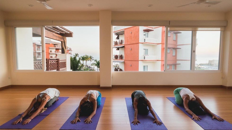 People in yoga class, stretching on mats in front of windows with a view.