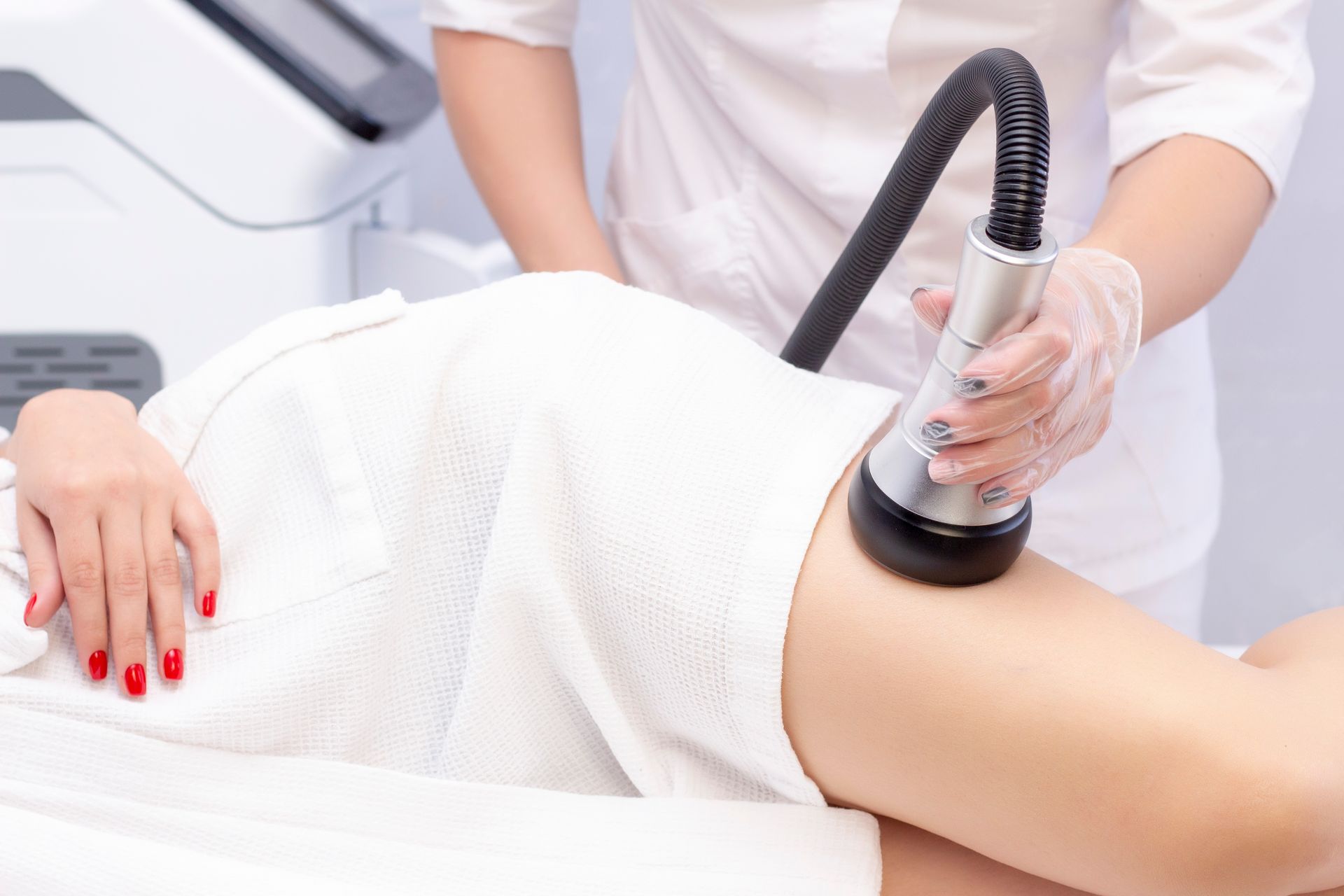 A technician uses a handheld cosmetic device on a person's upper thigh during a spa treatment.