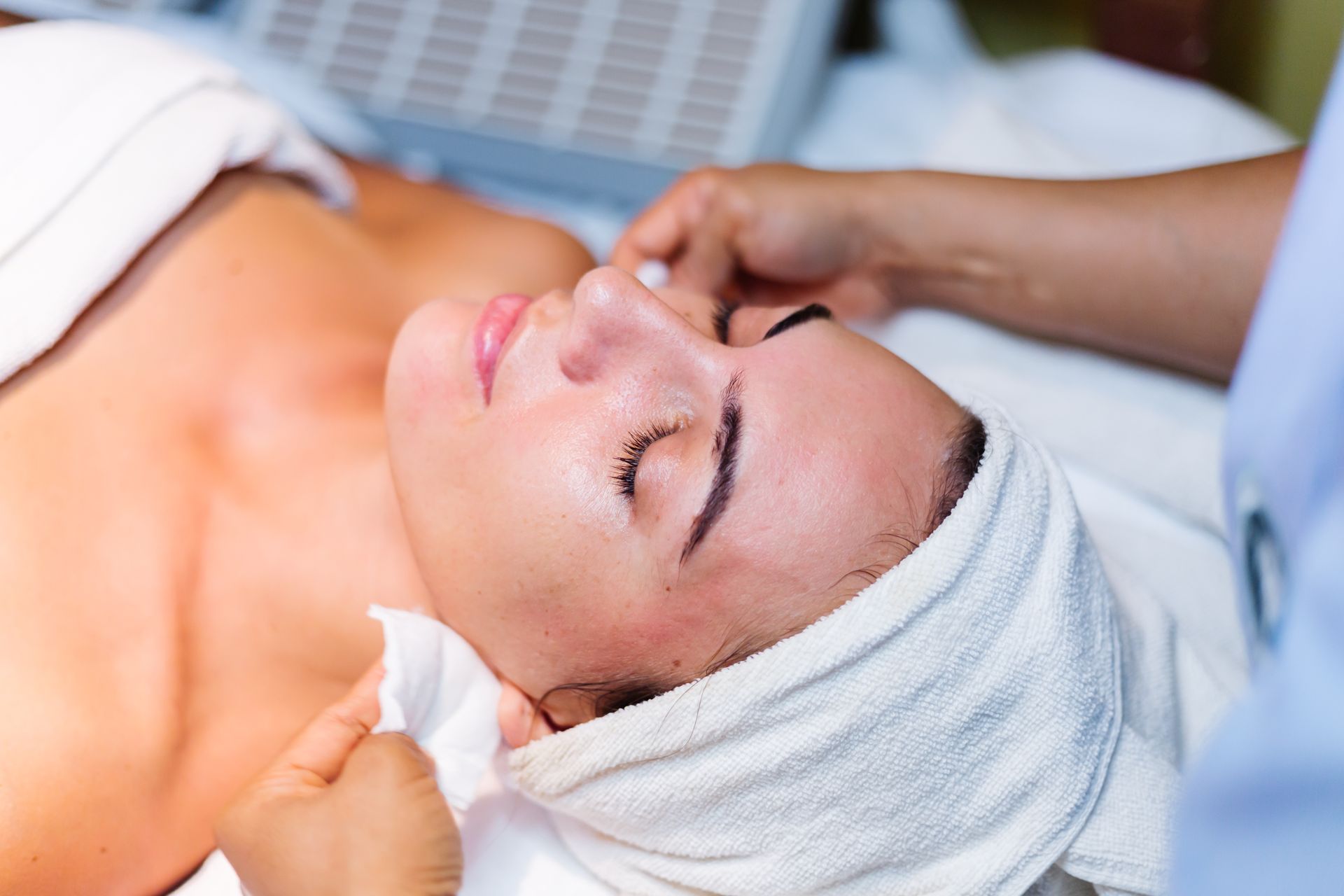 Woman receiving a facial treatment with a towel wrapped around her head and eyes closed