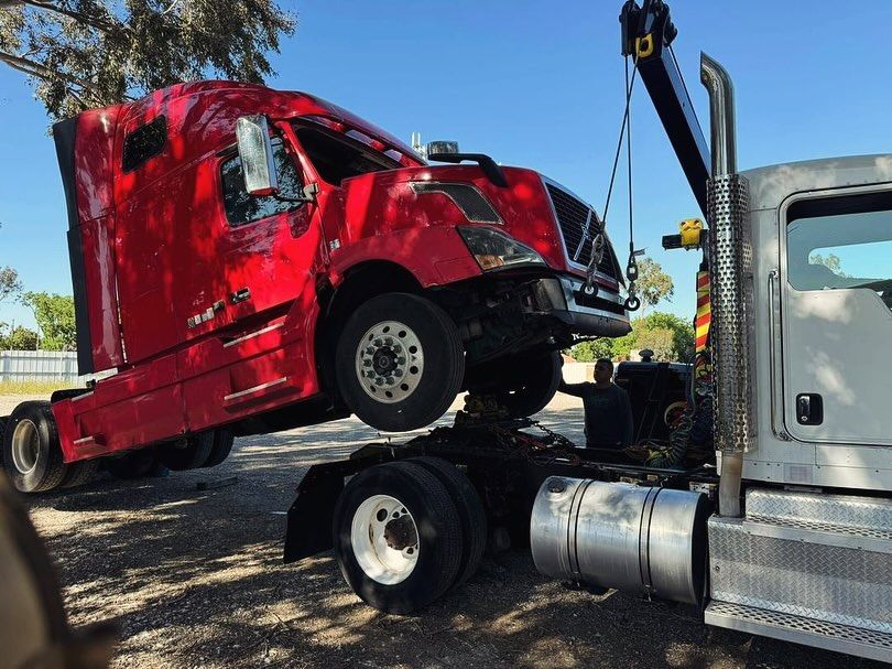 Heavy wrecker lifting the front of a red sleeper-cab semi tractor