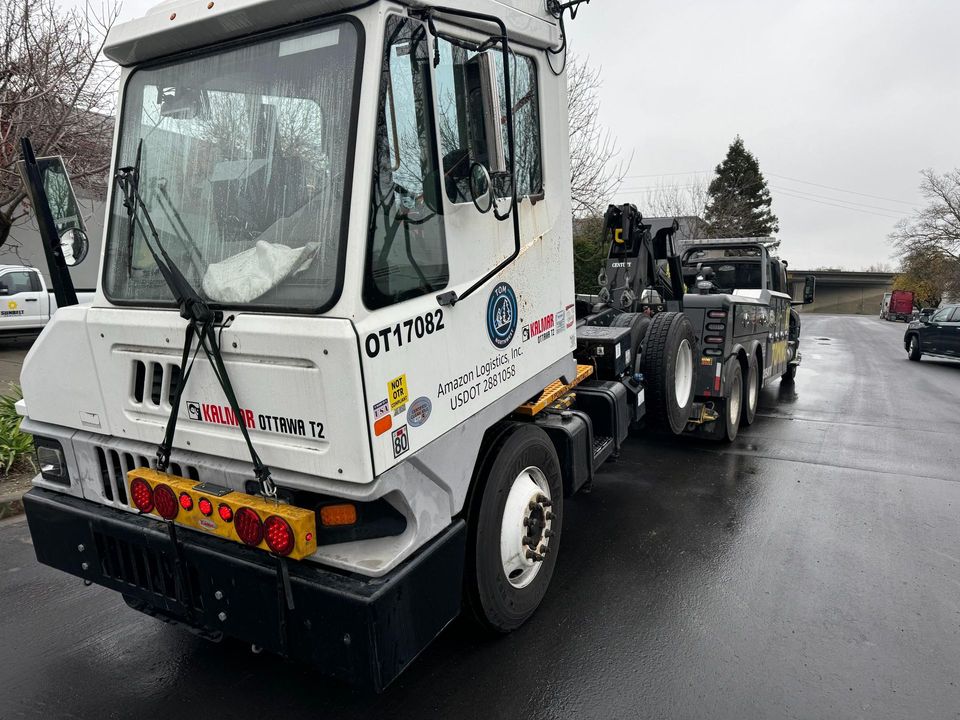 AT Towing wrecker hooked to a white yard spotter tractor on a wet street