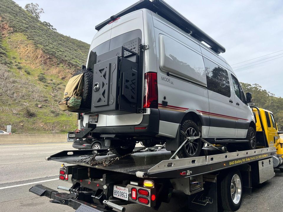 Silver Sprinter camper van secured on an AT Towing flatbed beside a hillside
