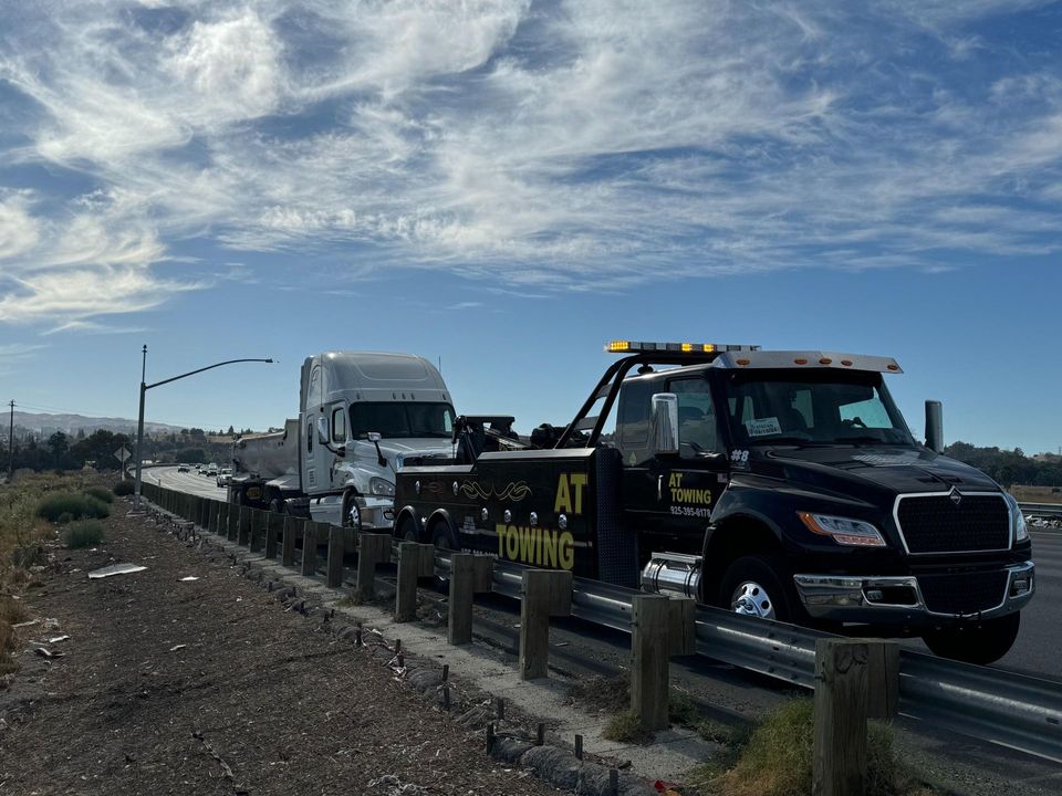 Black AT Towing wrecker towing a white semi tractor along a Bay Area highway