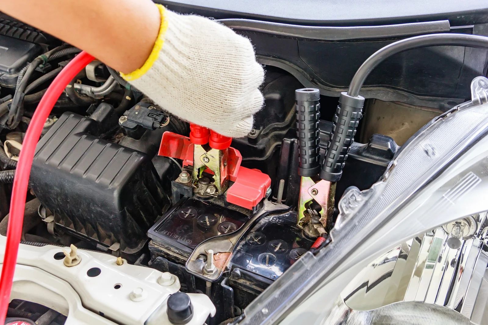 Gloved hands connecting jumper cables to a car battery in the engine bay