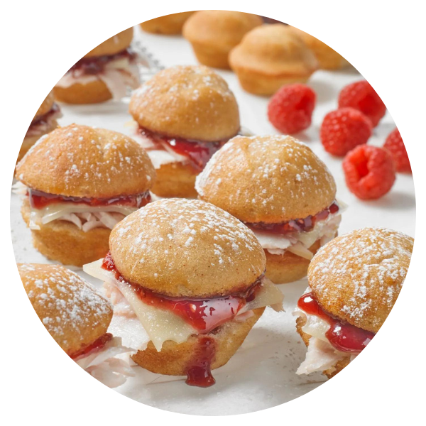 A bunch of mini hamburgers with raspberries in the background