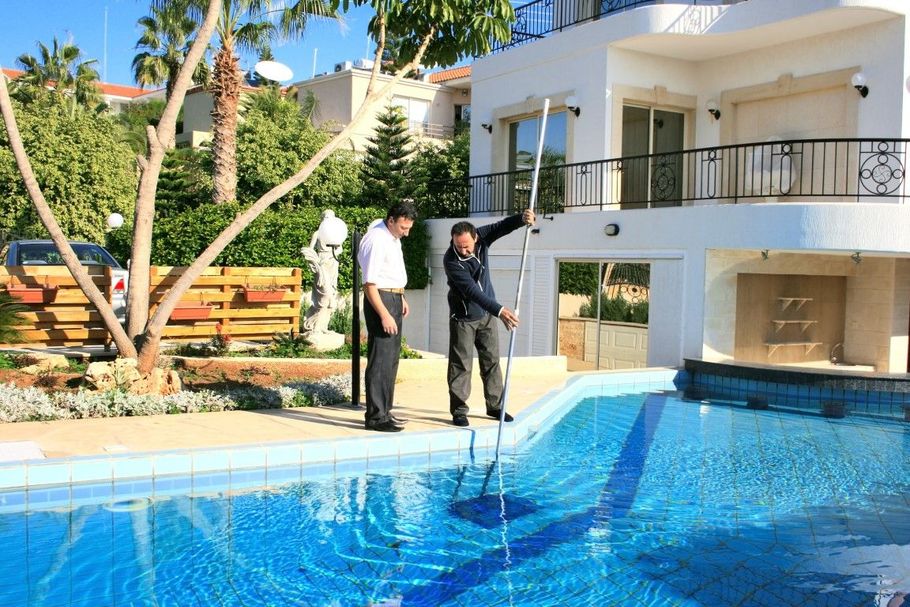 Two people by a blue swimming pool outside a white villa on a sunny day
