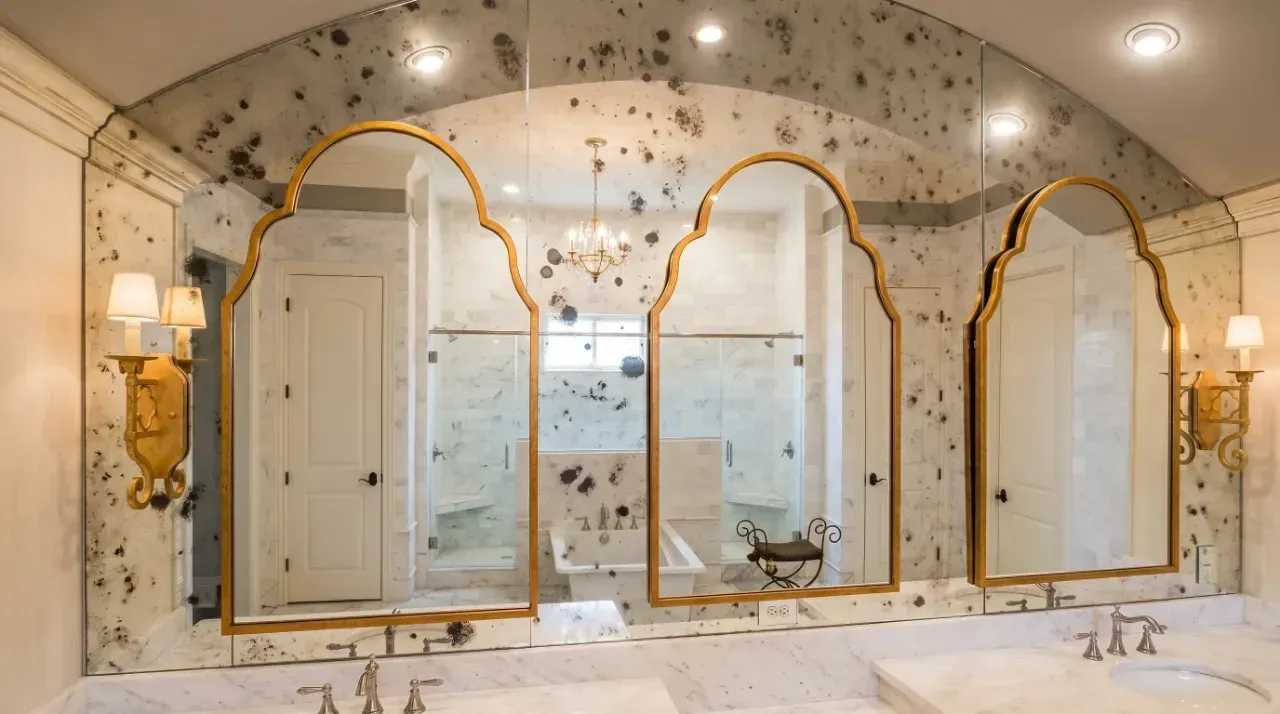 Elegant marble bathroom with gold-trimmed arched mirrors and sconces over a double vanity.