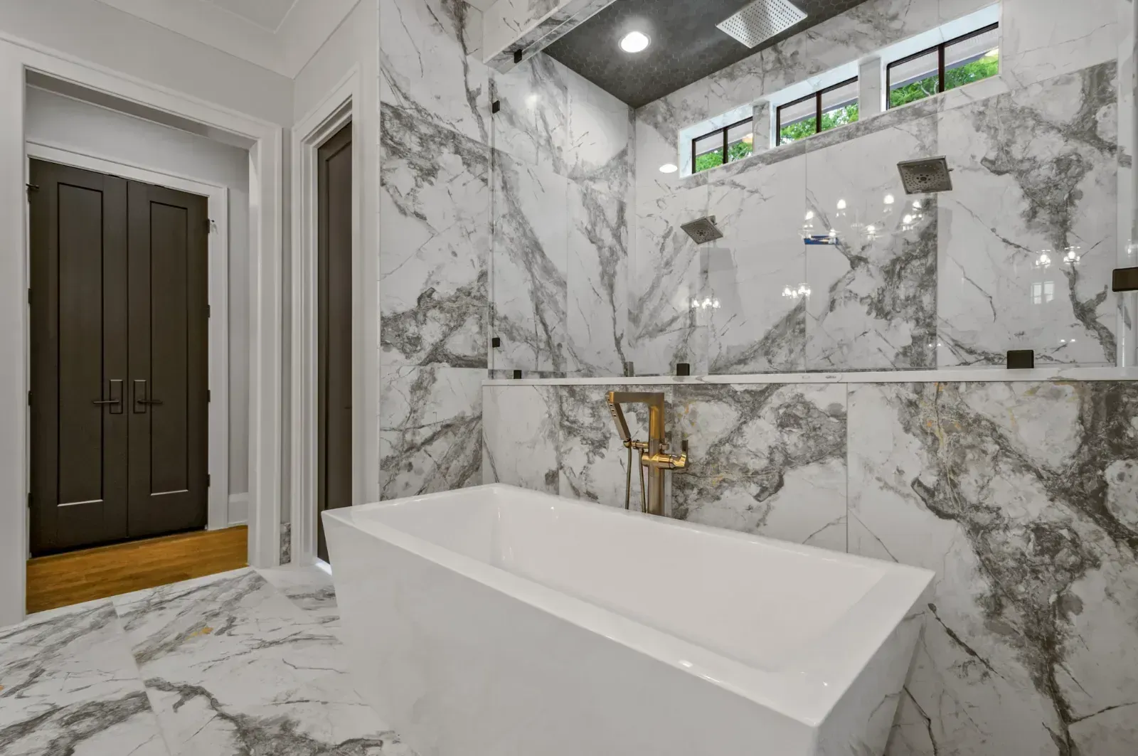 Modern marble bathroom with freestanding tub, glass shower, and high window.