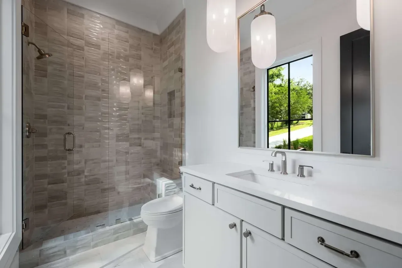 Modern bathroom with walk-in shower, white vanity, and window overlooking greenery