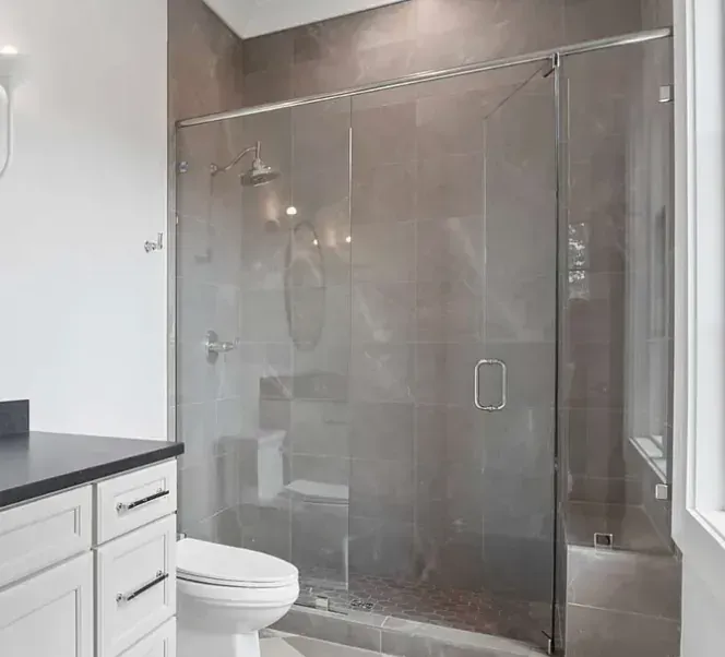 Modern bathroom with glass shower enclosure, white vanity, and toilet beside a marble-look wall