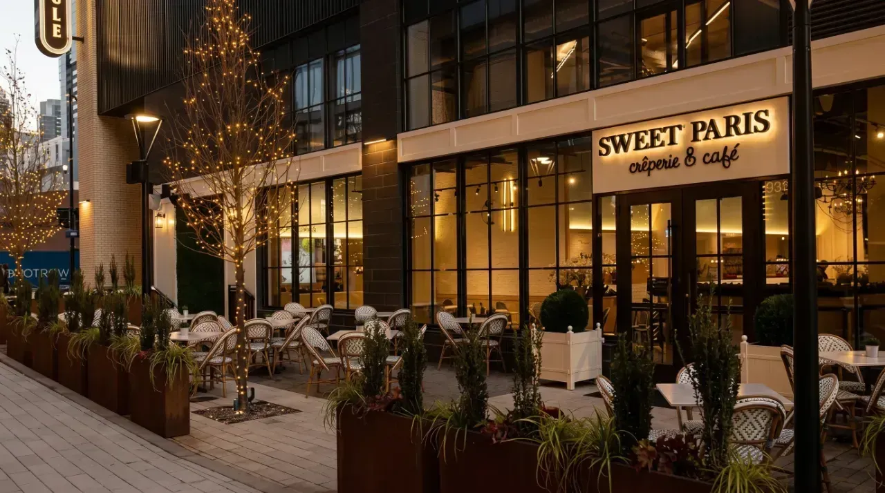 Outdoor café seating outside Sweet Paris in a warmly lit city street at dusk