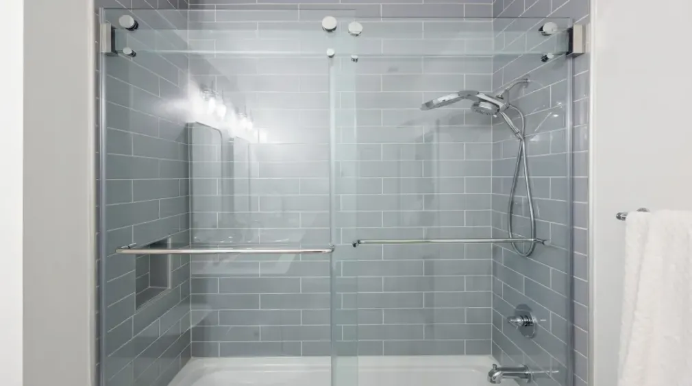 Accessible walk-in shower with gray tile, glass doors, built-in bench, and grab bars