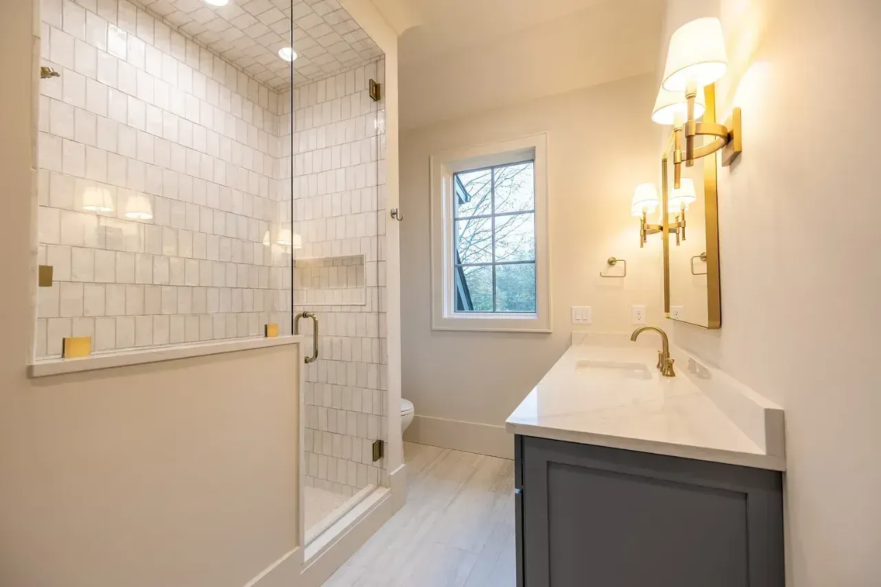 Bright white bathroom with tiled shower, vanity, mirror sconces, and a window