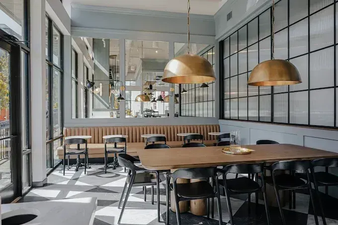 Modern cafe interior with wooden tables, black chairs, pendant lights, and large windows
