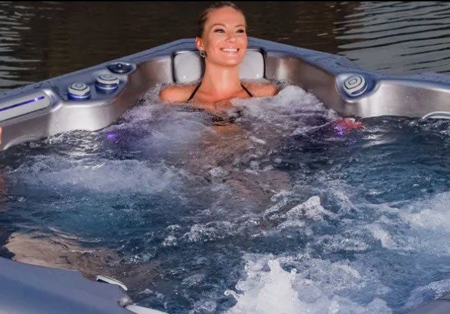 Woman in black bikini relaxing in bubbly blue hot tub, smiling.