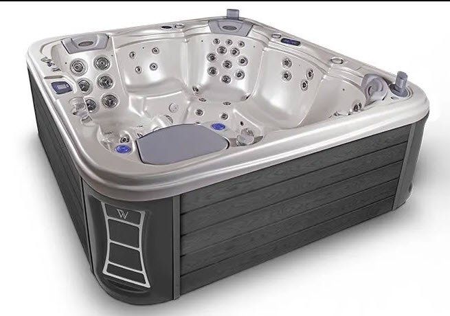 Gray hot tub with seating and jets against gray-brown composite siding.