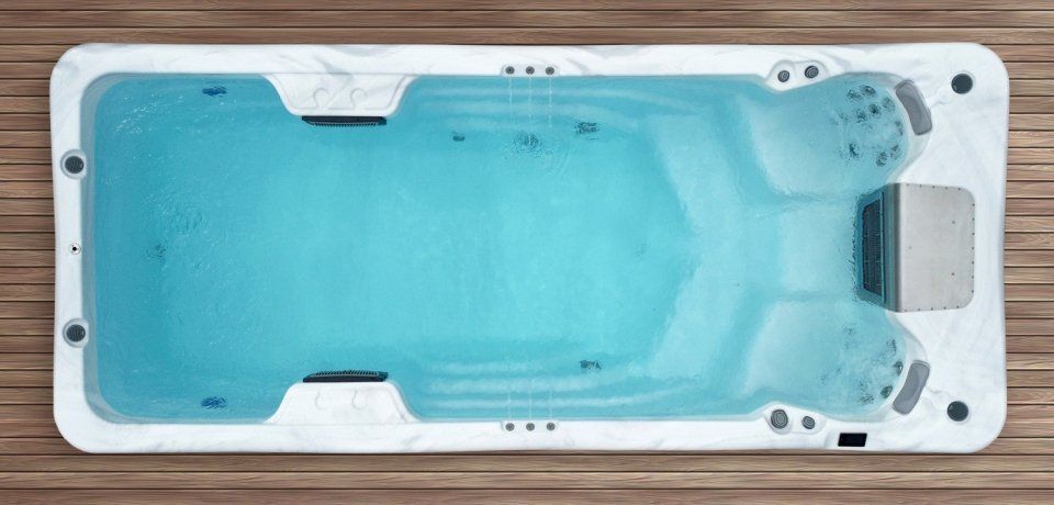 Top-down view of a rectangular swim spa with blue water and white trim, on wooden decking.
