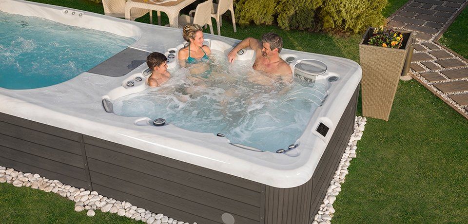 A family enjoys a swim spa with jets. They are splashing and having fun in the water.