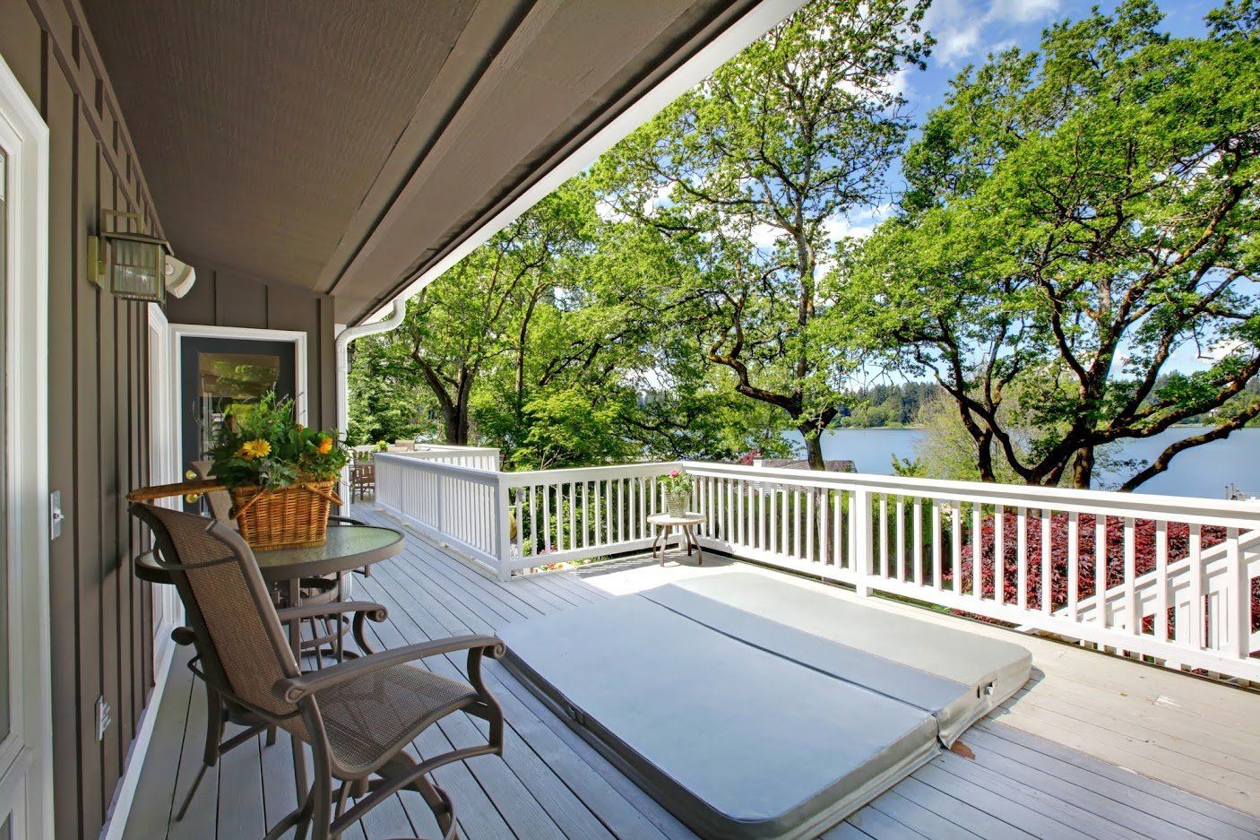 Deck with a hot tub and seating overlooking a lake and trees.