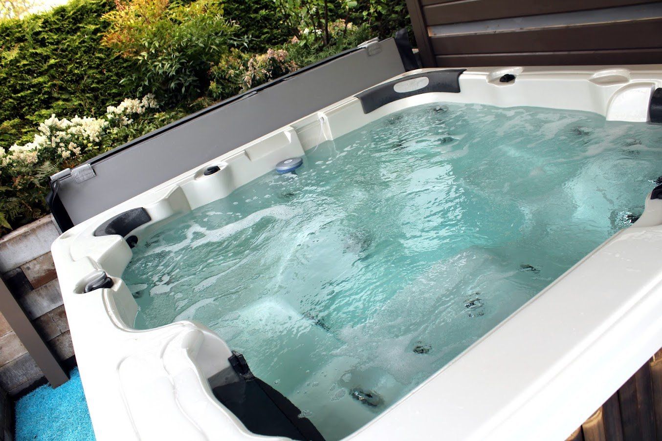 A bubbling hot tub filled with clear water, set outside next to lush greenery.
