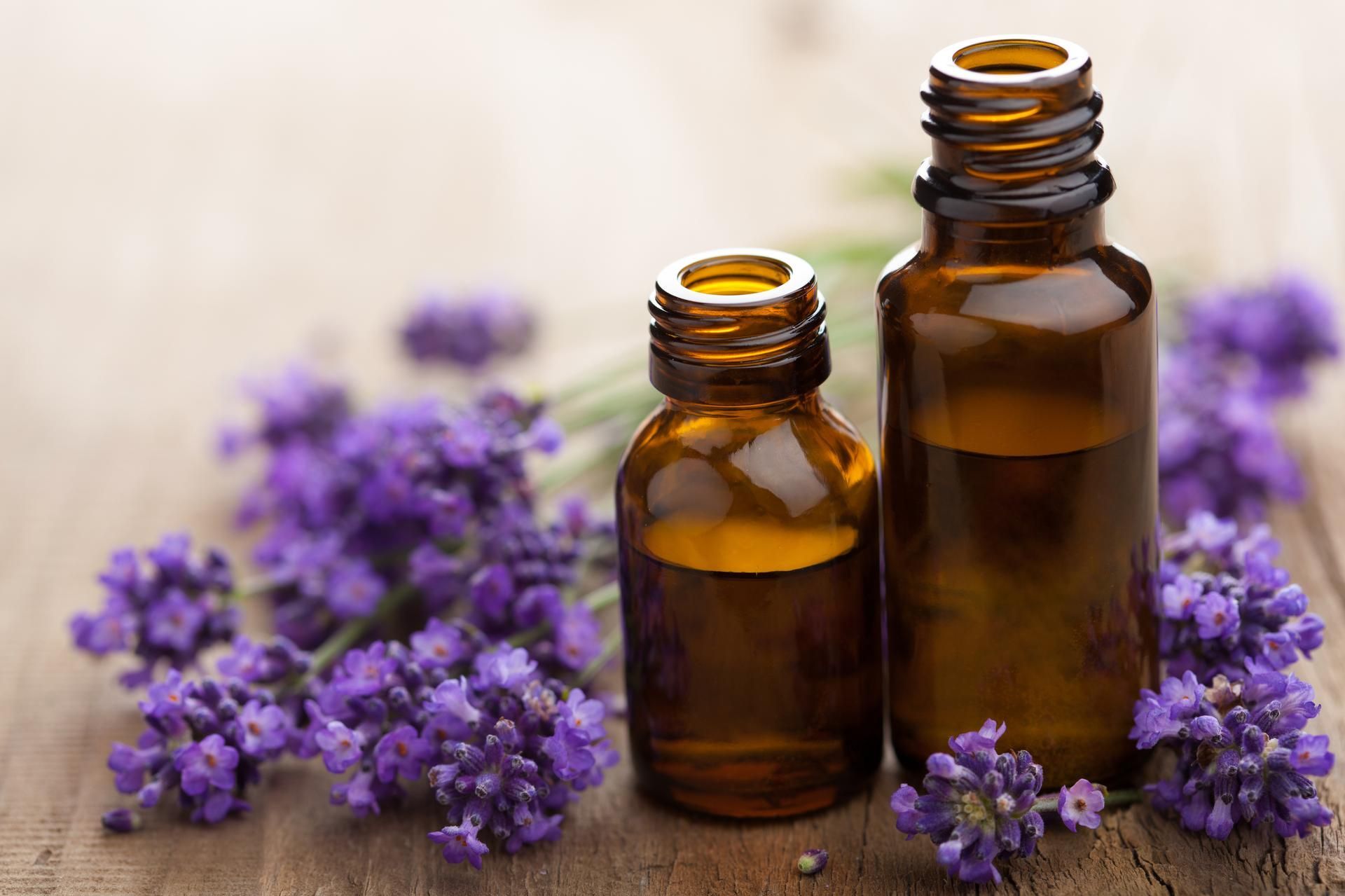 Two amber essential oil bottles with purple lavender on a wooden surface.