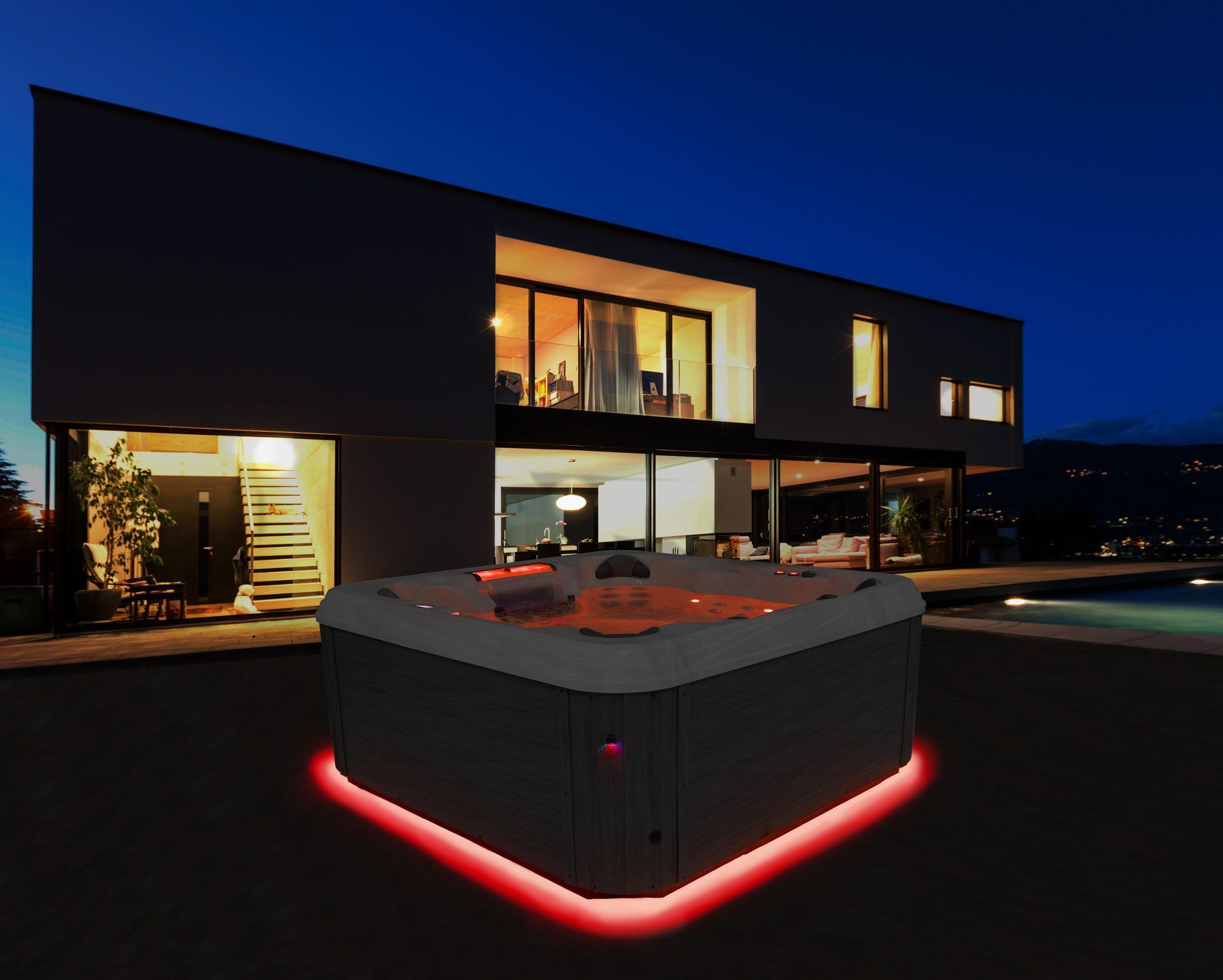 A square hot tub with red LED base lighting sits on a patio at night in front of a modern home.