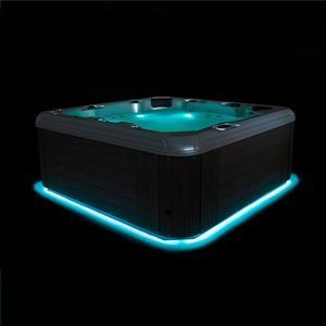 A square dark-paneled hot tub glows with teal interior lighting and a bright neon blue light strip at its base.