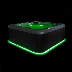 A square hot tub illuminated by bright green internal and base lighting against a solid black background.