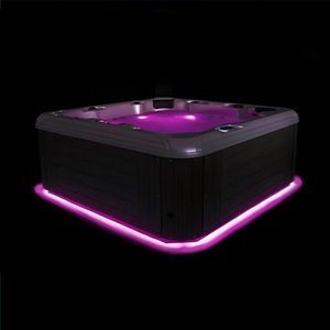 A square hot tub with dark gray siding, glowing with vibrant purple interior and base lighting against a black background.