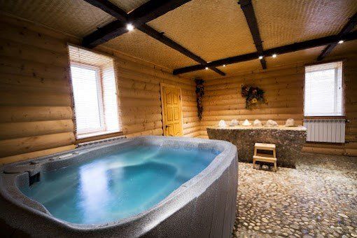 Log cabin spa with a large blue hot tub, wooden walls and ceiling, pebble floor.